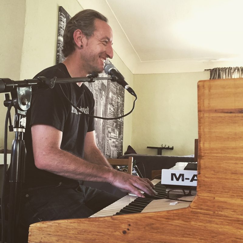 Gary smiling at the piano, singing into a mic